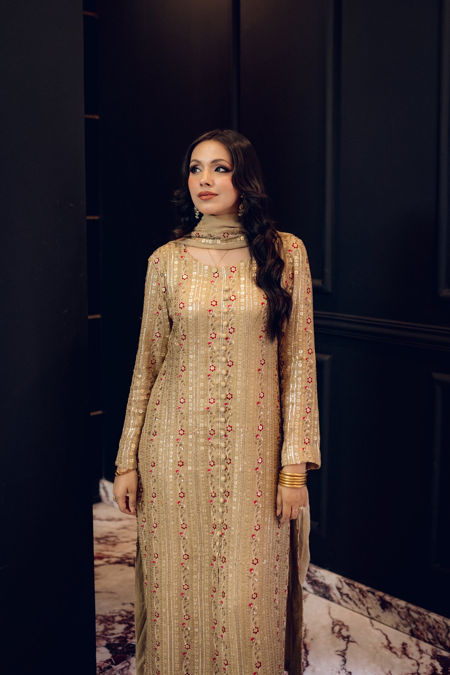 A luxurious and sophisticated dress featuring golden sequin shimmer, intricate multithread embroidery, refined buttons, a chiffon dupatta with embroidered borders and sequins, and flared raw silk pants—perfect for making a statement at special occasions.