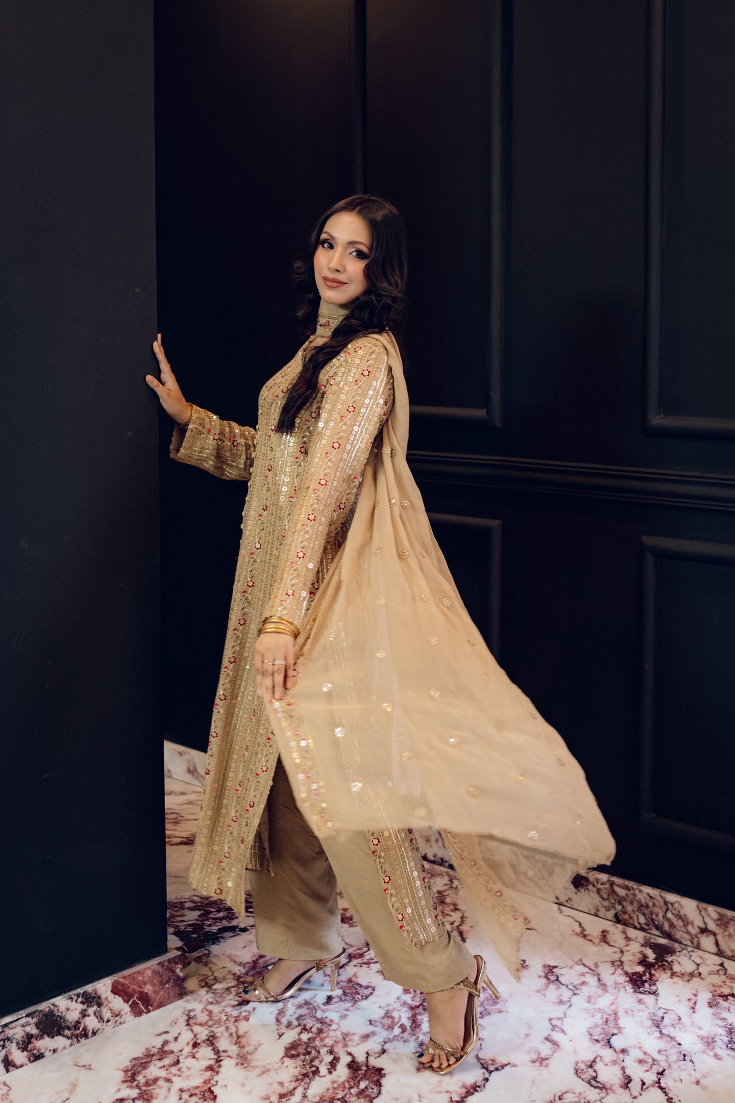 A luxurious and sophisticated dress featuring golden sequin shimmer, intricate multithread embroidery, refined buttons, a chiffon dupatta with embroidered borders and sequins, and flared raw silk pants—perfect for making a statement at special occasions.