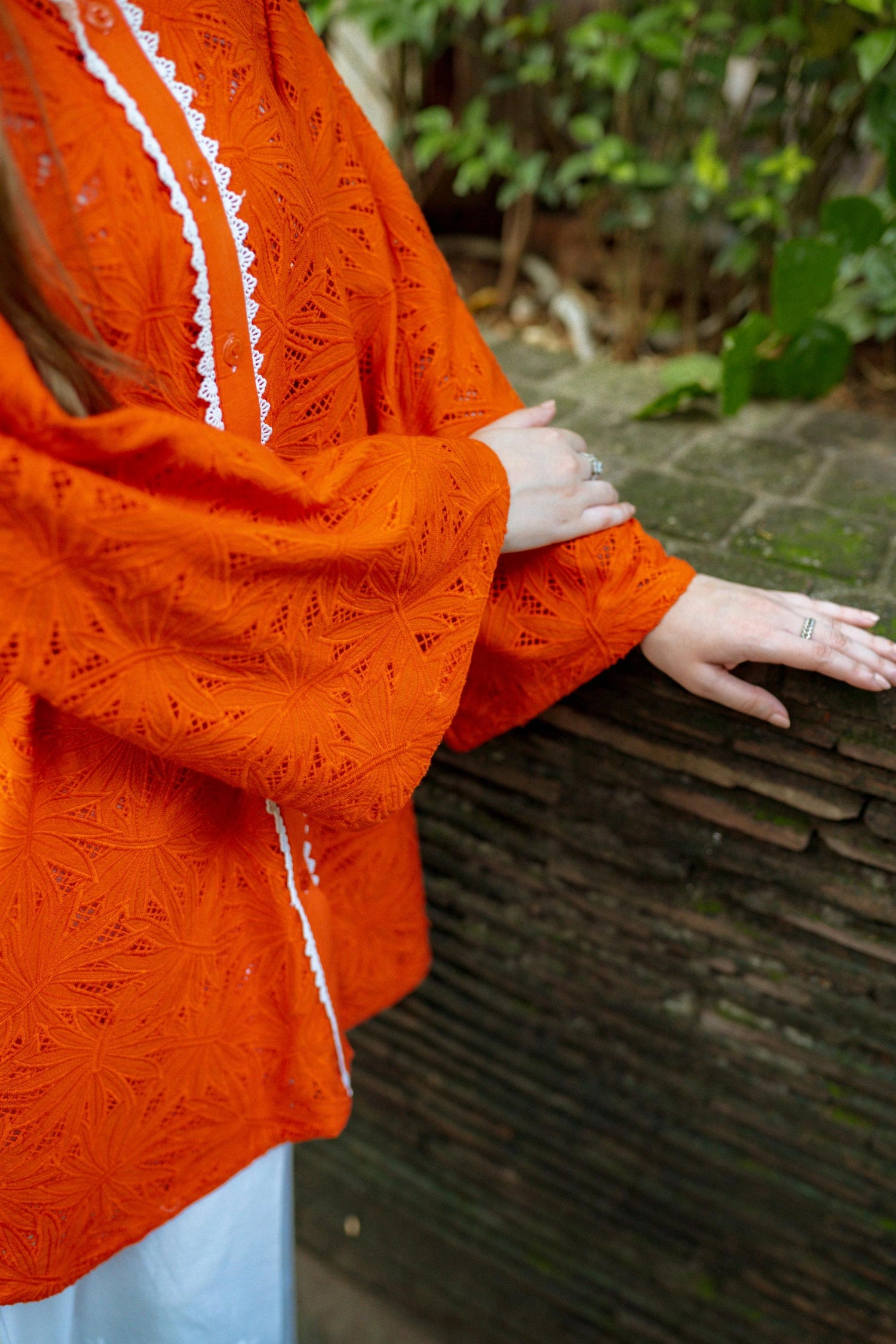 Stylish blunt orange short button-down shirt with a refined collar, contemporary round hem, and intricate lace along the buttons.