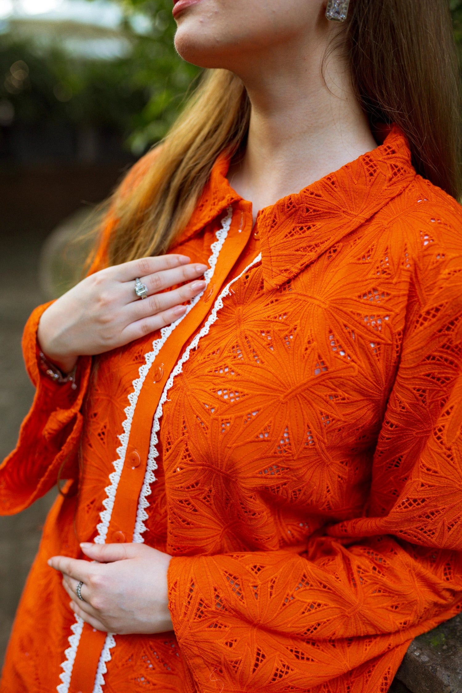 Stylish blunt orange short button-down shirt with a refined collar, contemporary round hem, and intricate lace along the buttons.