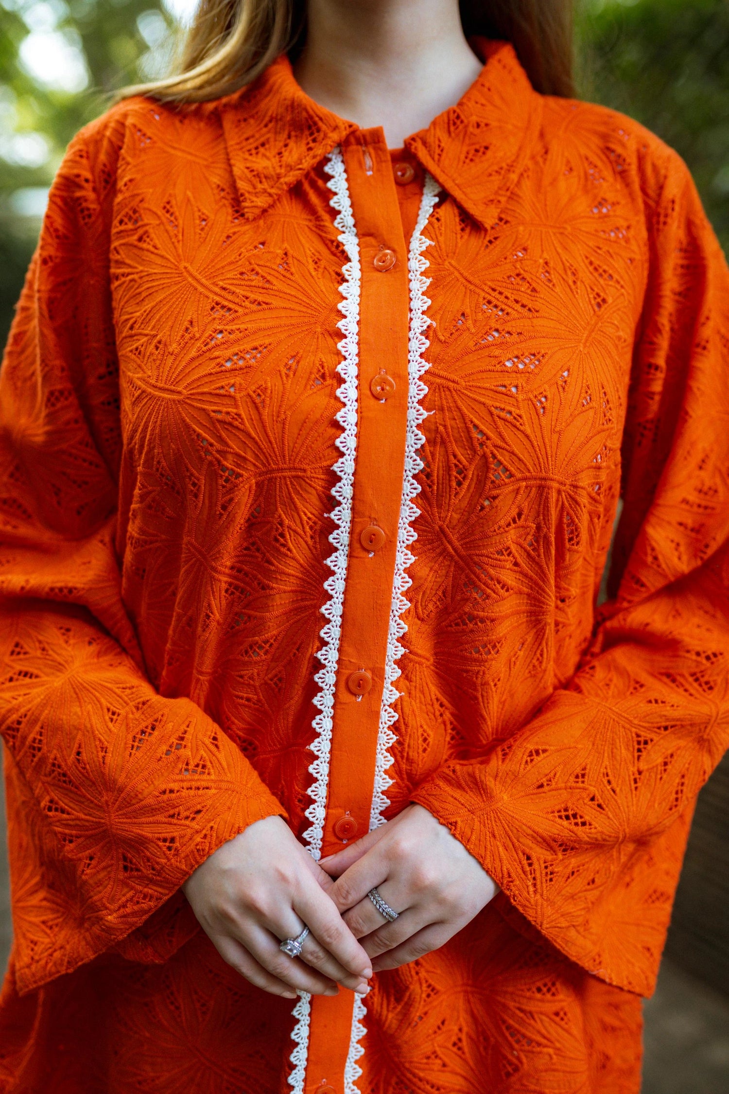 Stylish blunt orange short button-down shirt with a refined collar, contemporary round hem, and intricate lace along the buttons.