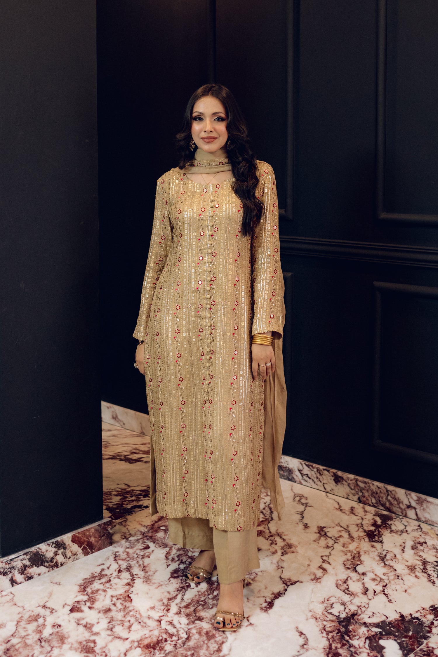 A luxurious and sophisticated dress featuring golden sequin shimmer, intricate multithread embroidery, refined buttons, a chiffon dupatta with embroidered borders and sequins, and flared raw silk pants—perfect for making a statement at special occasions.