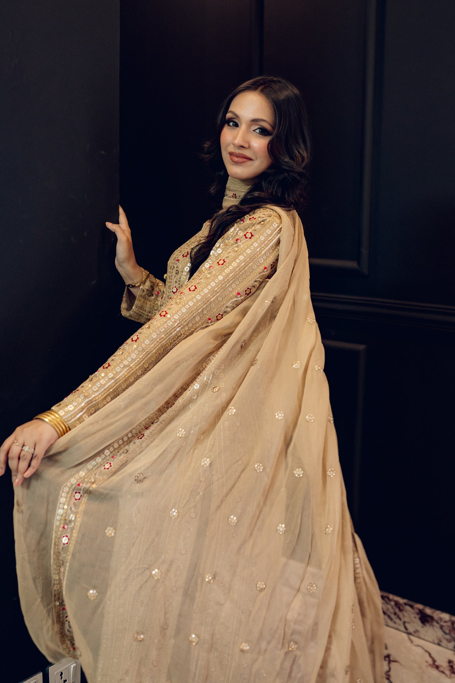 A luxurious and sophisticated dress featuring golden sequin shimmer, intricate multithread embroidery, refined buttons, a chiffon dupatta with embroidered borders and sequins, and flared raw silk pants—perfect for making a statement at special occasions.