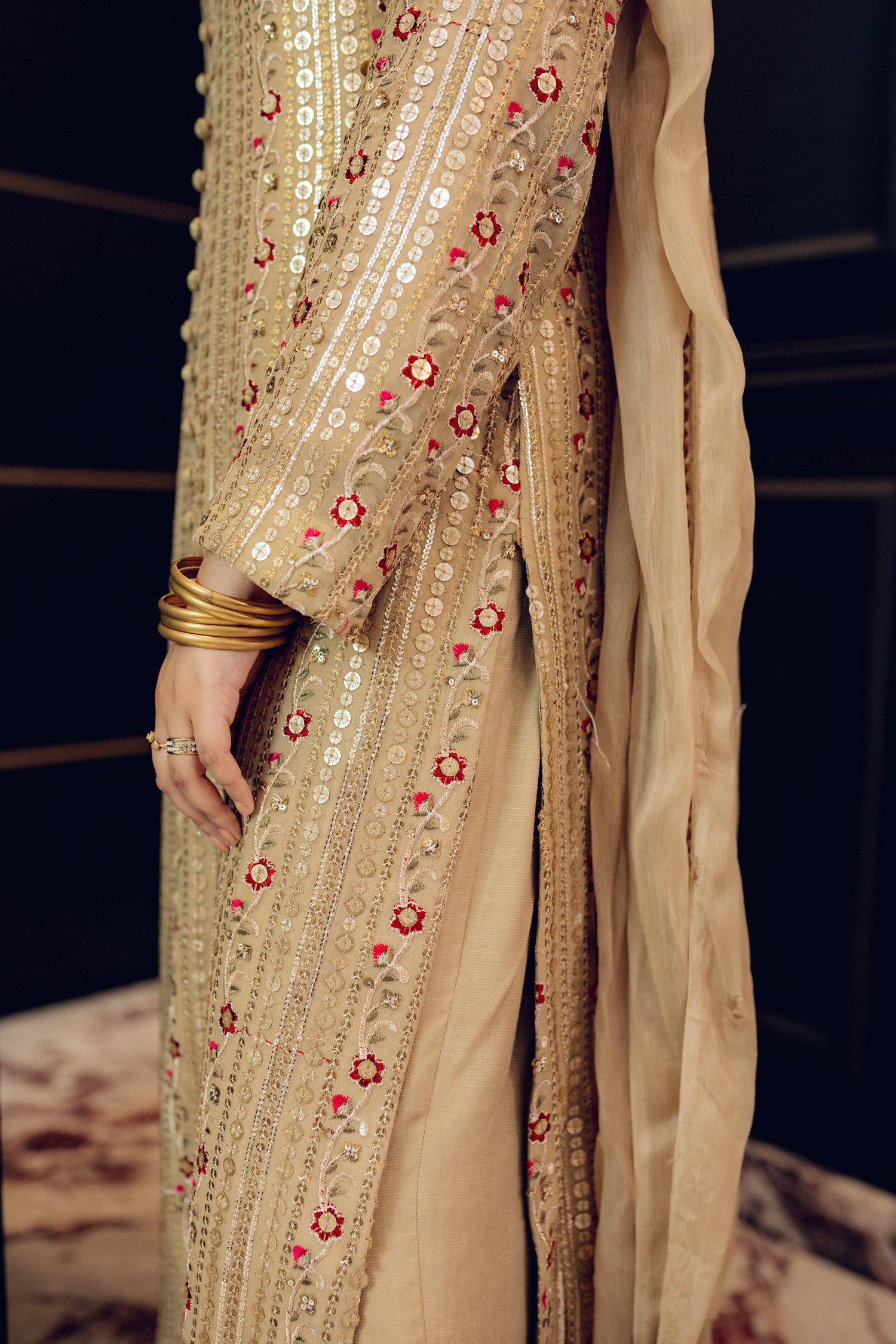 A luxurious and sophisticated dress featuring golden sequin shimmer, intricate multithread embroidery, refined buttons, a chiffon dupatta with embroidered borders and sequins, and flared raw silk pants—perfect for making a statement at special occasions.