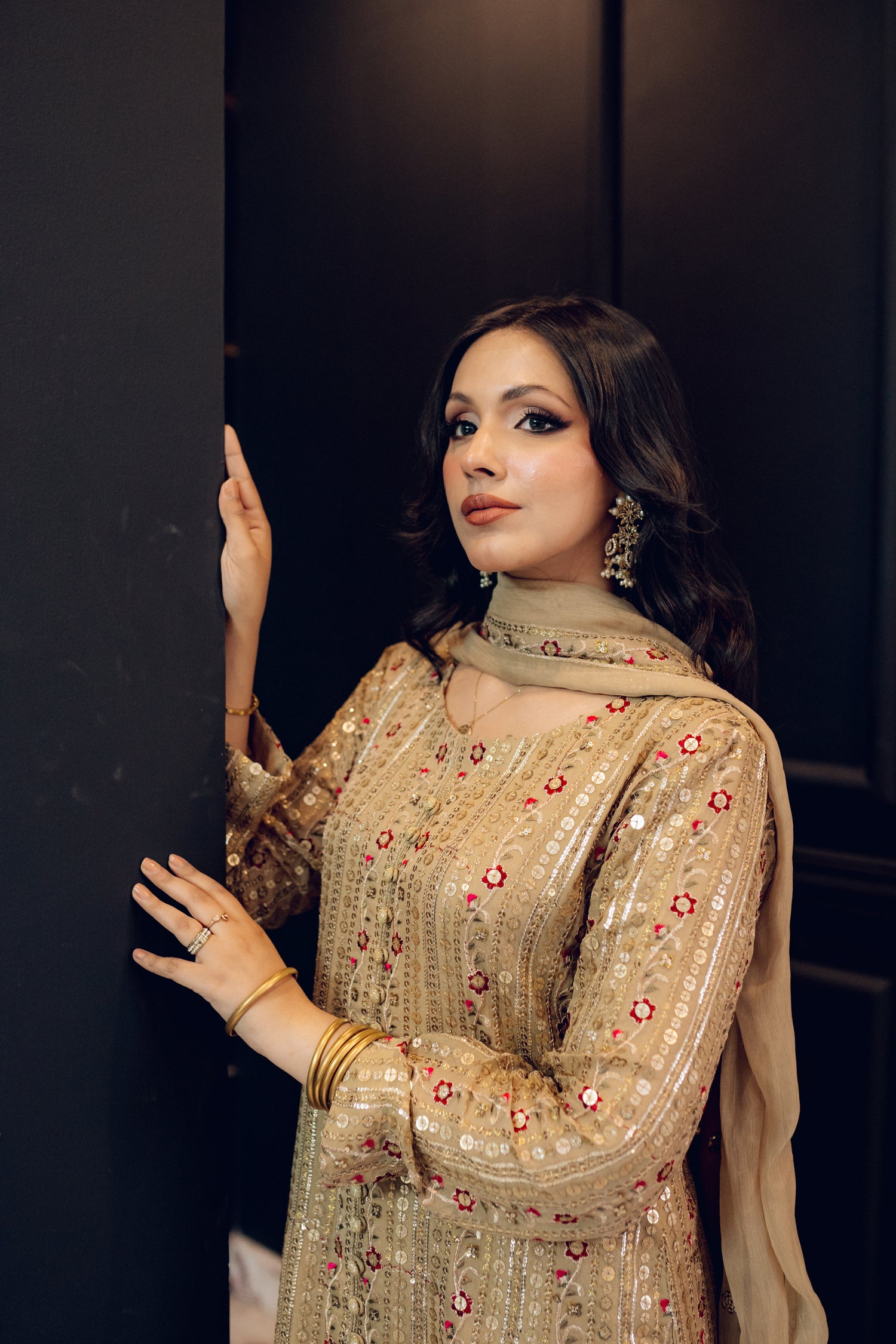 A luxurious and sophisticated dress featuring golden sequin shimmer, intricate multithread embroidery, refined buttons, a chiffon dupatta with embroidered borders and sequins, and flared raw silk pants—perfect for making a statement at special occasions.