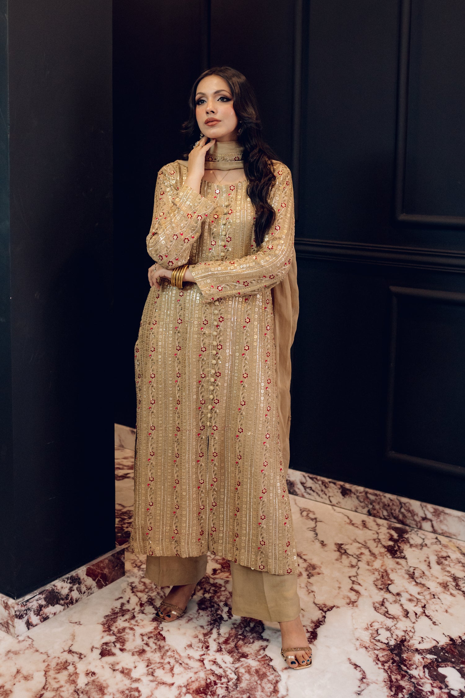 A luxurious and sophisticated dress featuring golden sequin shimmer, intricate multithread embroidery, refined buttons, a chiffon dupatta with embroidered borders and sequins, and flared raw silk pants—perfect for making a statement at special occasions.