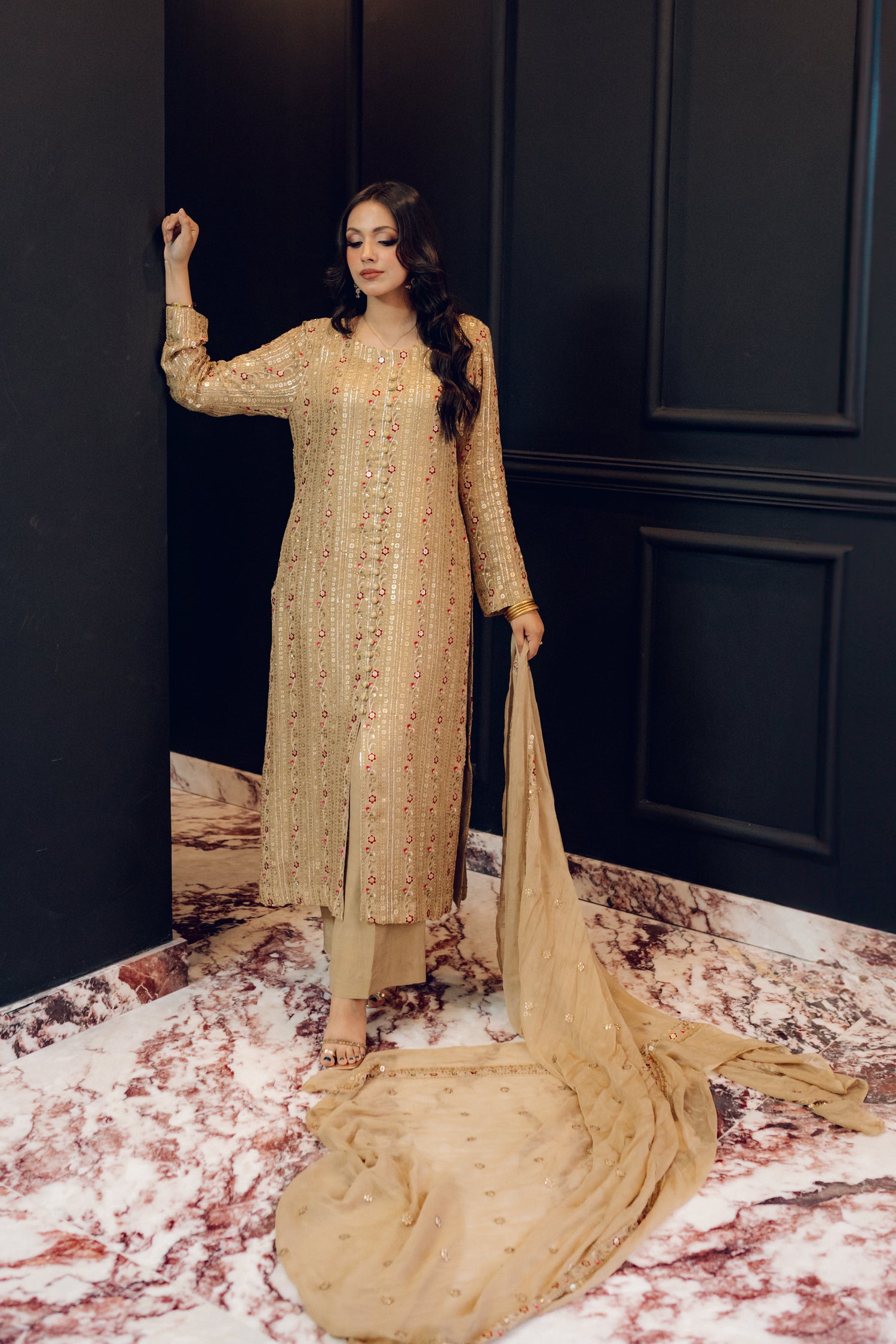 A luxurious and sophisticated dress featuring golden sequin shimmer, intricate multithread embroidery, refined buttons, a chiffon dupatta with embroidered borders and sequins, and flared raw silk pants—perfect for making a statement at special occasions.