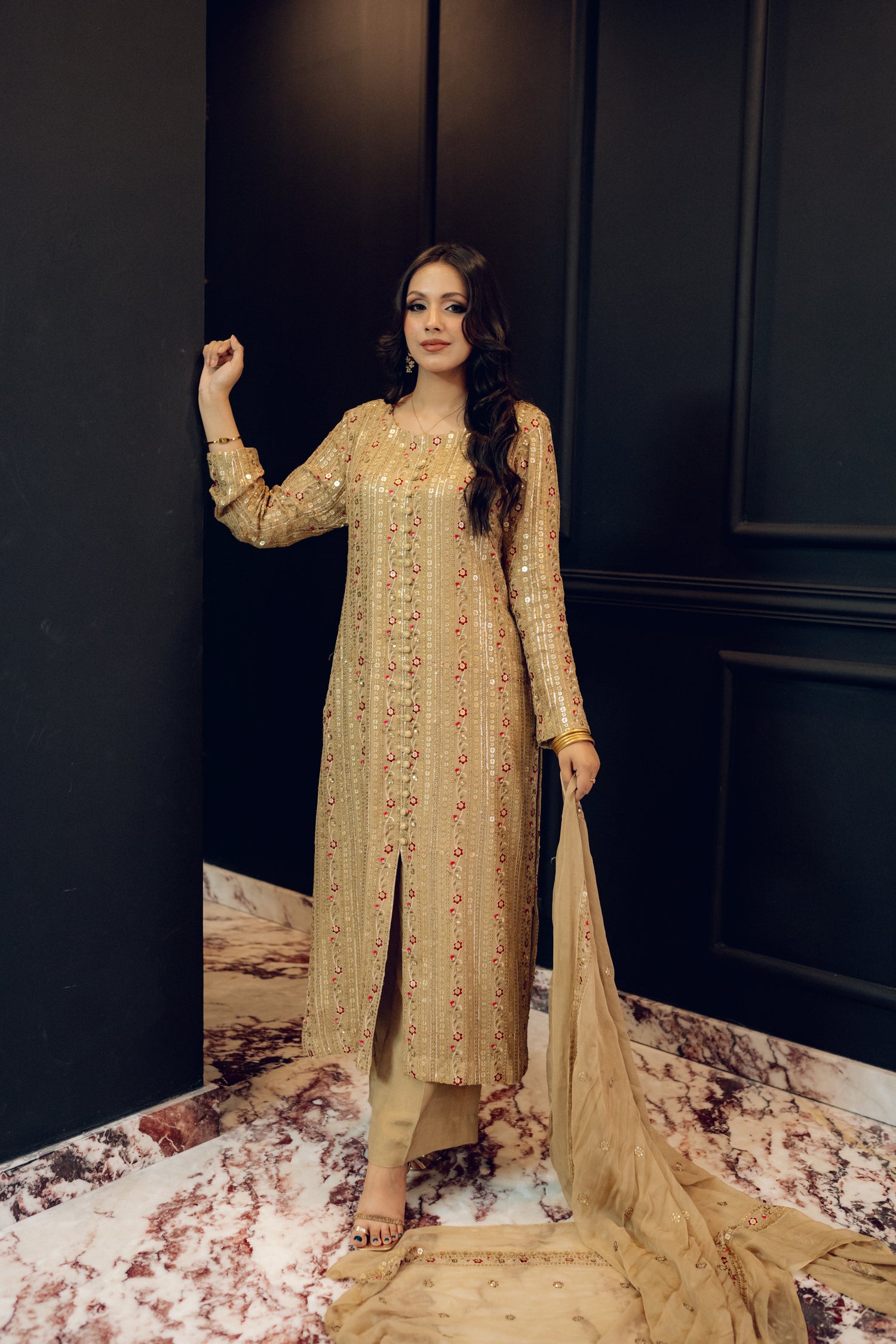 A luxurious and sophisticated dress featuring golden sequin shimmer, intricate multithread embroidery, refined buttons, a chiffon dupatta with embroidered borders and sequins, and flared raw silk pants—perfect for making a statement at special occasions.