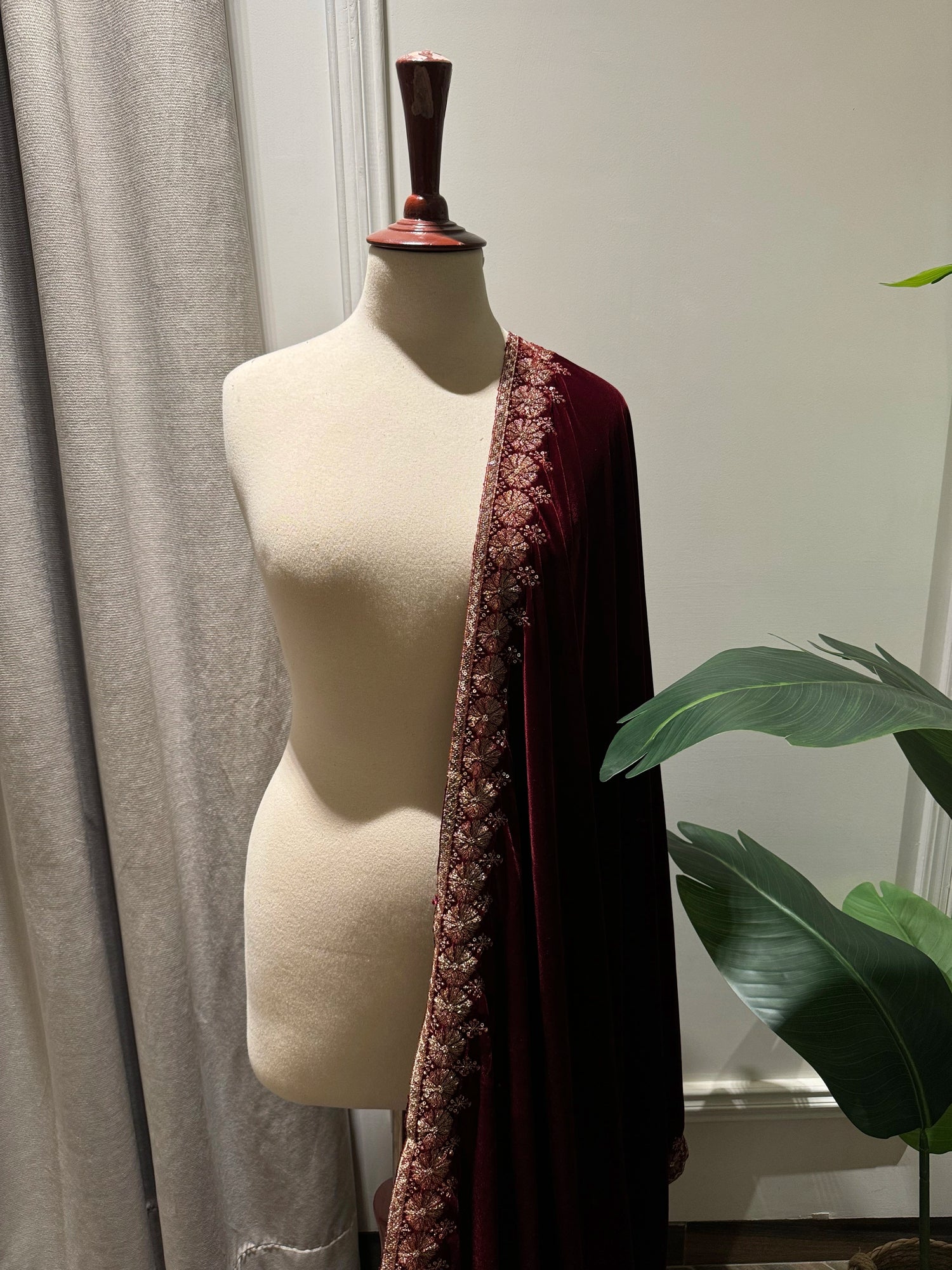 Exquisite deep maroon velvet shawl with wide antique gold tilla embroidery and sequins forming intricate floral motifs along scalloped edges, perfect for formal winter occasions.