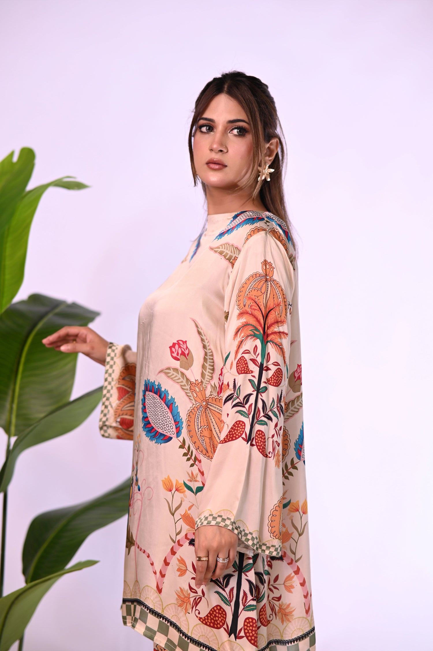 Cord Set in skin gold silk featuring a long tunic with a structured high neckline and full sleeves. Paired with wide-leg culotte pants, both pieces are adorned with colorful botanical motifs.