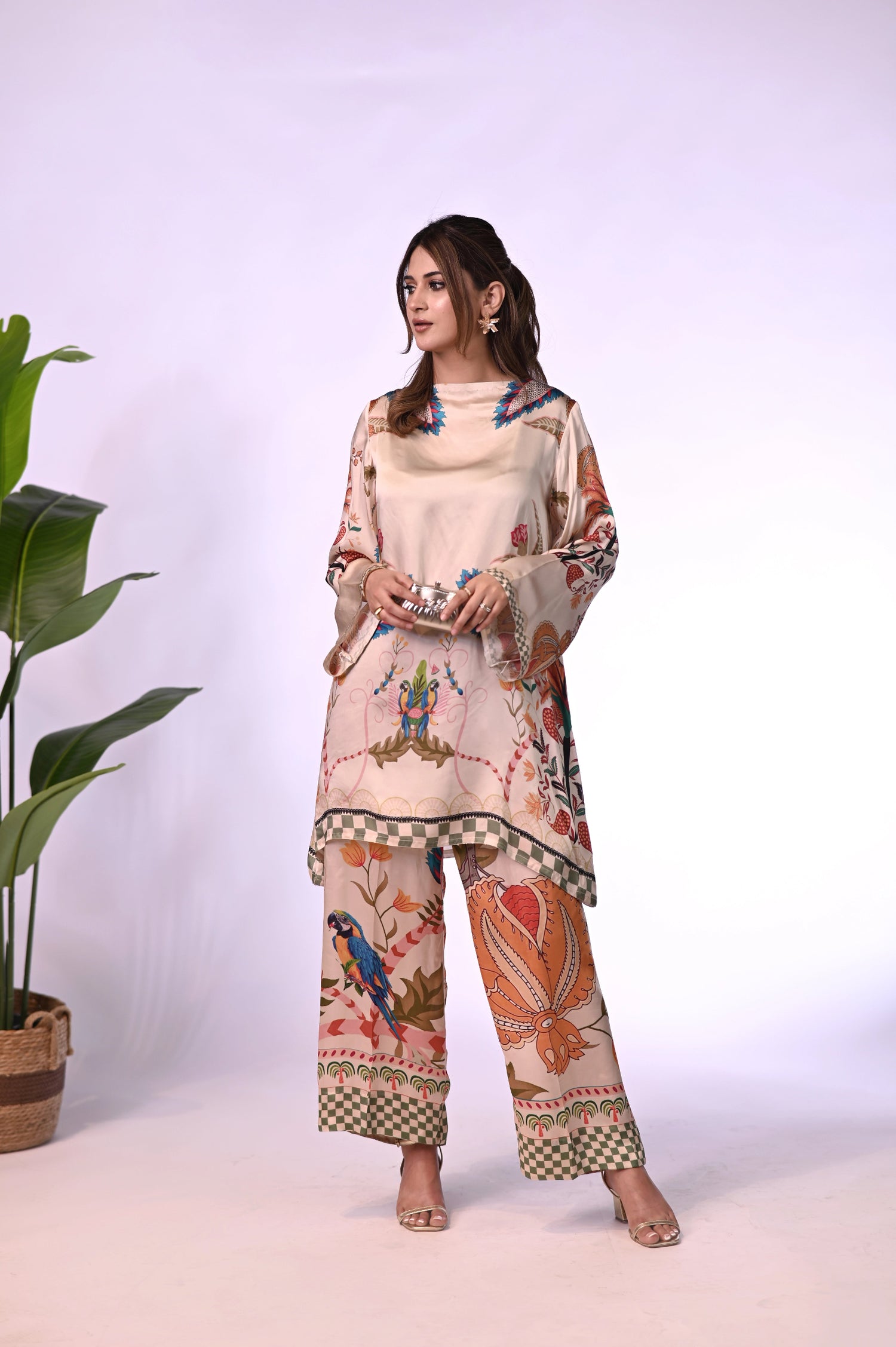 Cord Set in skin gold silk featuring a long tunic with a structured high neckline and full sleeves. Paired with wide-leg culotte pants, both pieces are adorned with colorful botanical motifs.
