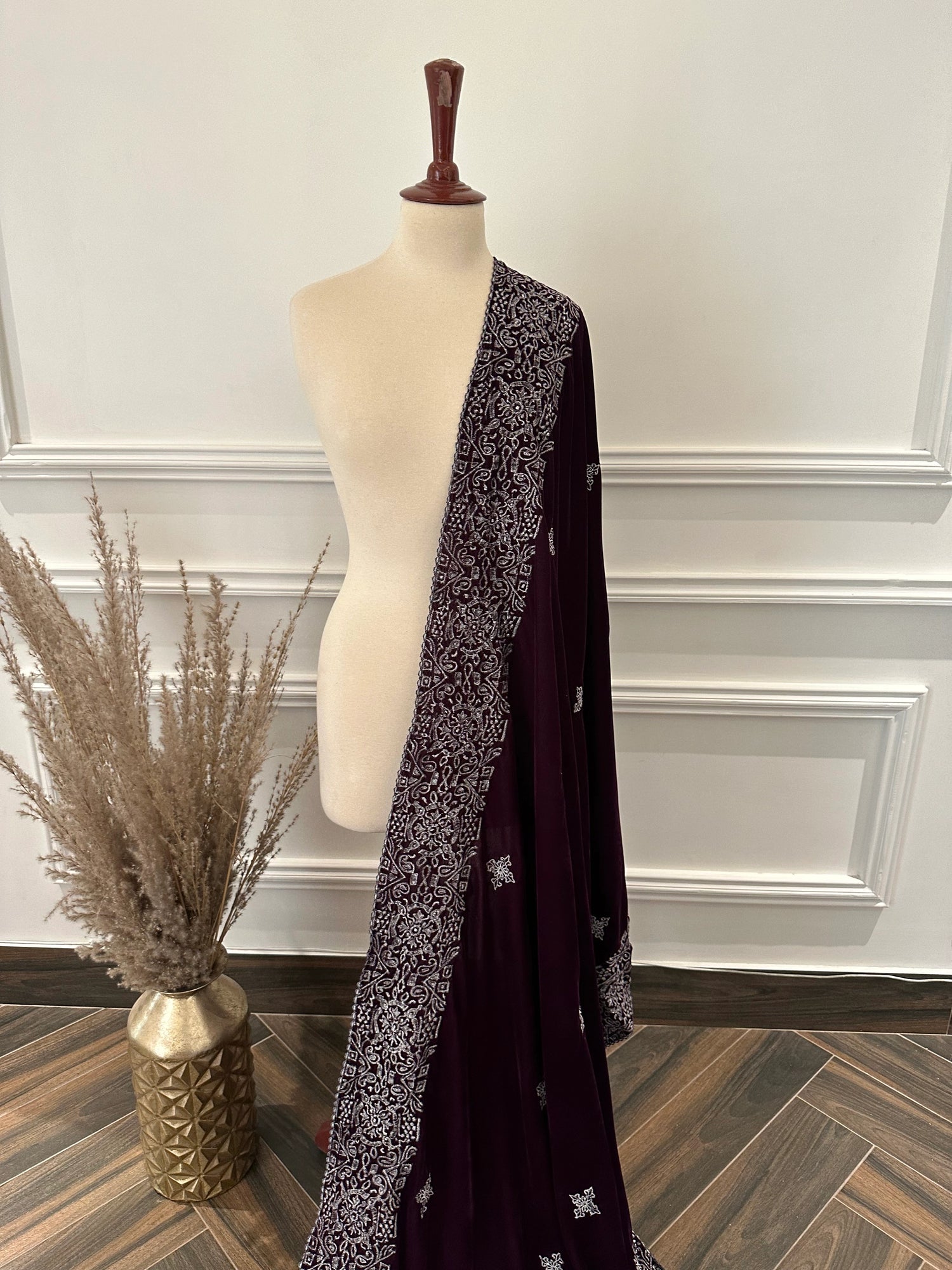 Rich deep plum velvet shawl with a smooth, lustrous finish, detailed with elaborate silver tilla embroidery. The shawl features a bold ornamental border of floral motifs across the body and finished with graceful border edges, making it a refined choice for formal occasions.
