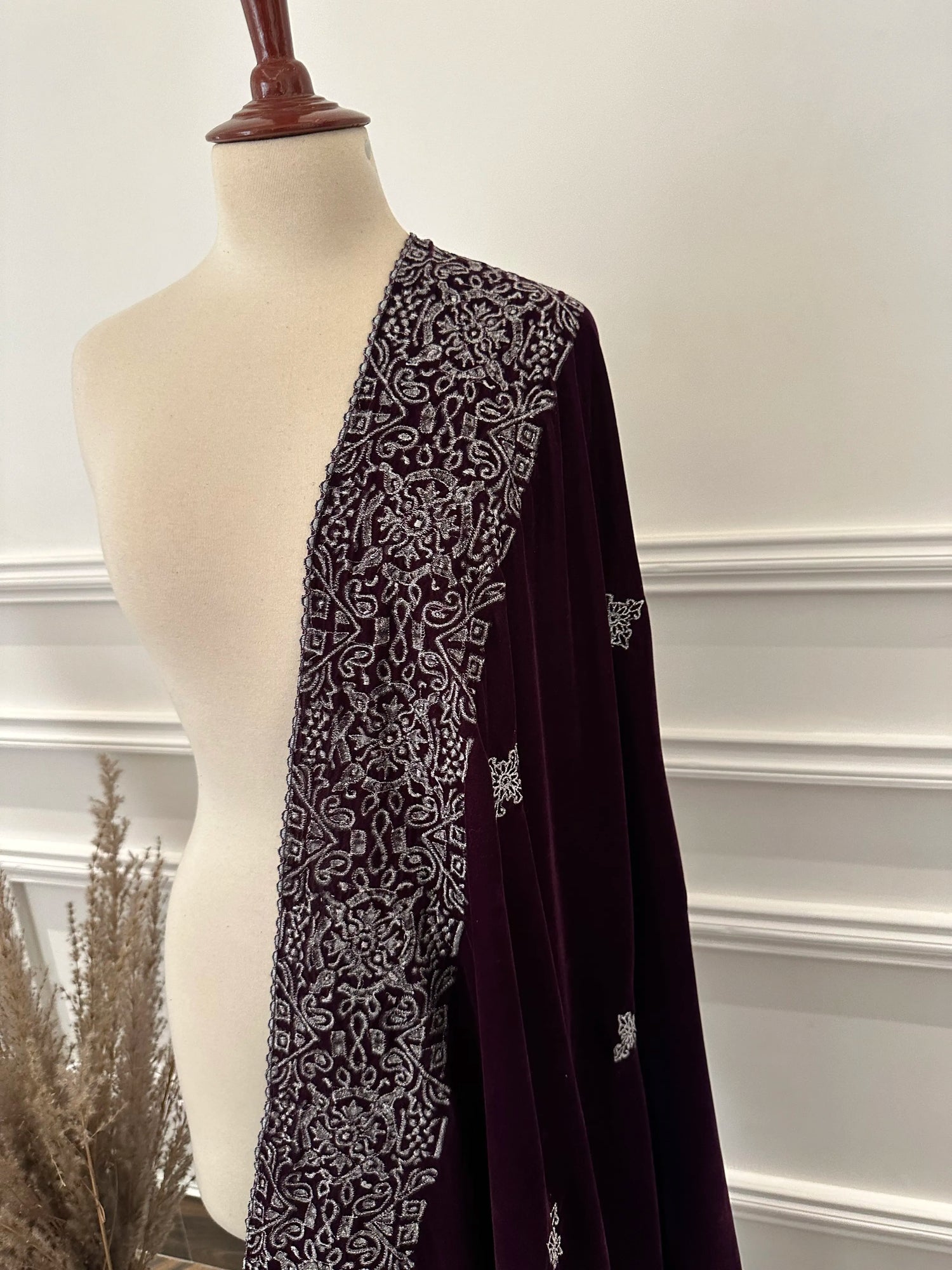 Rich deep plum velvet shawl with a smooth, lustrous finish, detailed with elaborate silver tilla embroidery. The shawl features a bold ornamental border of floral motifs across the body and finished with graceful border edges, making it a refined choice for formal occasions.