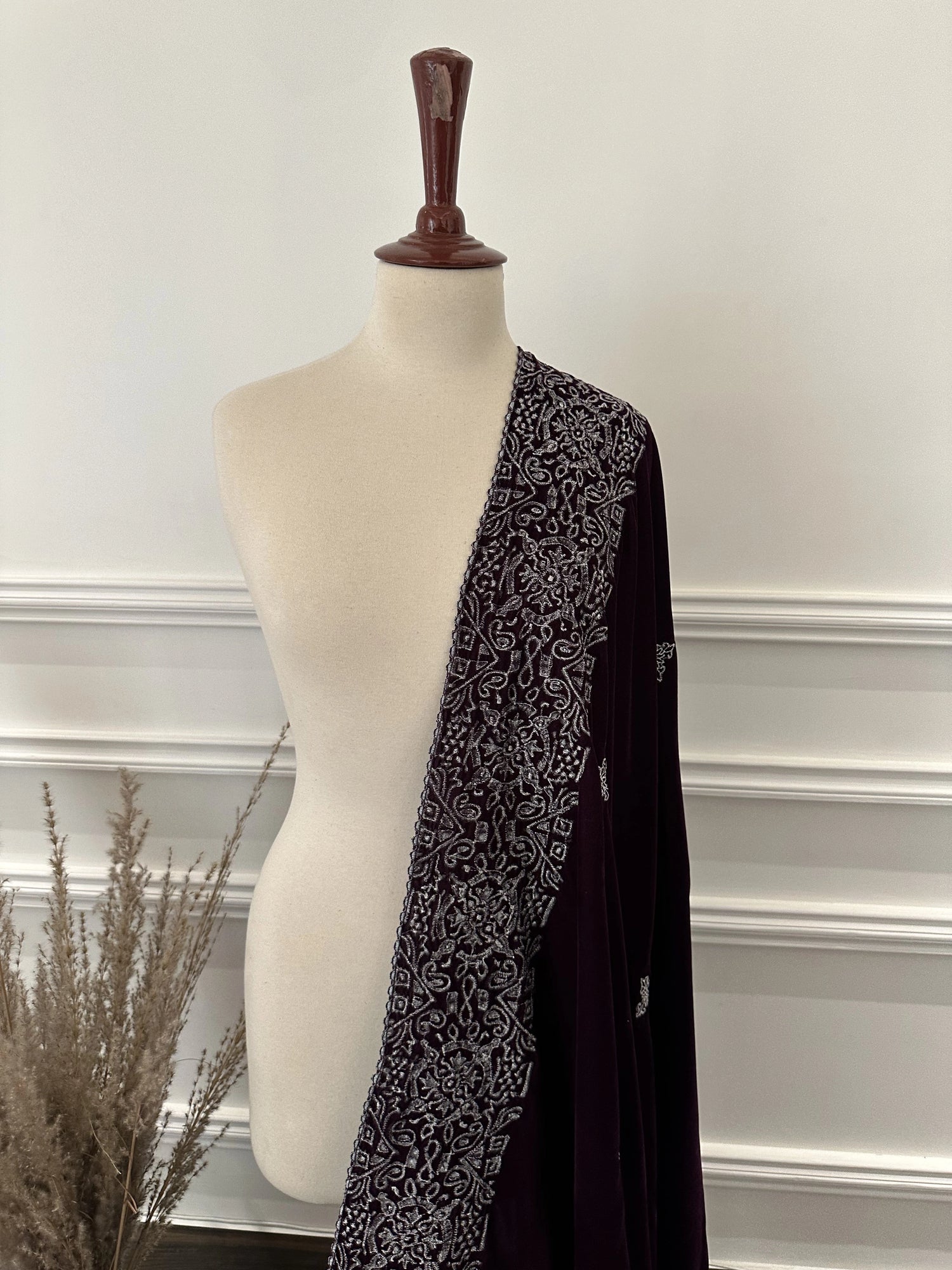 Rich deep plum velvet shawl with a smooth, lustrous finish, detailed with elaborate silver tilla embroidery. The shawl features a bold ornamental border of floral motifs across the body and finished with graceful border edges, making it a refined choice for formal occasions.