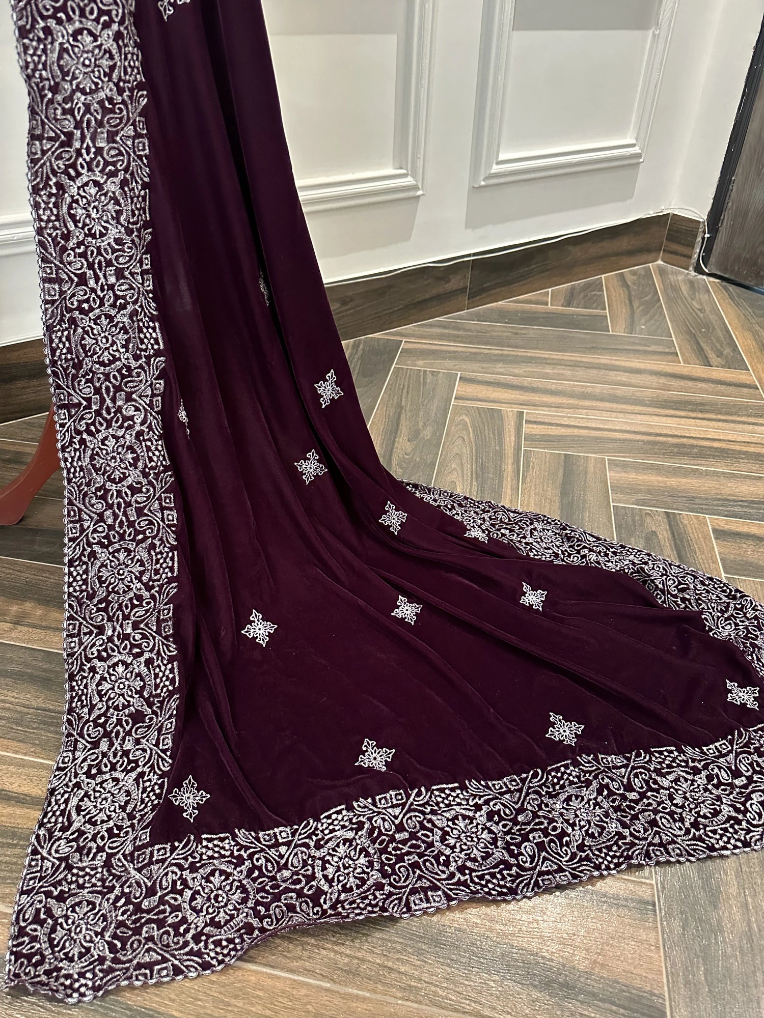 Rich deep plum velvet shawl with a smooth, lustrous finish, detailed with elaborate silver tilla embroidery. The shawl features a bold ornamental border of floral motifs across the body and finished with graceful border edges, making it a refined choice for formal occasions.
