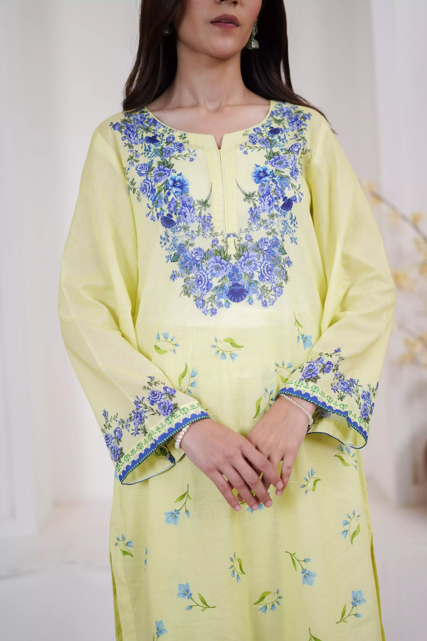 A pastel yellow suit adorned with delicate blue flowers and soft green leaves. The design features a border elegance and freshness.