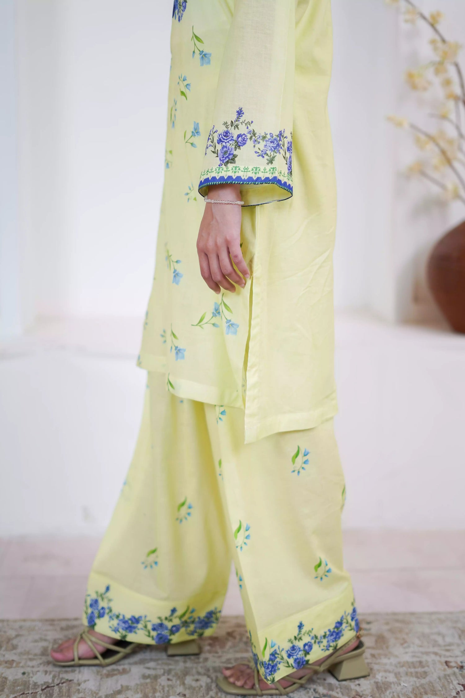 A pastel yellow suit adorned with delicate blue flowers and soft green leaves. The design features a border elegance and freshness.