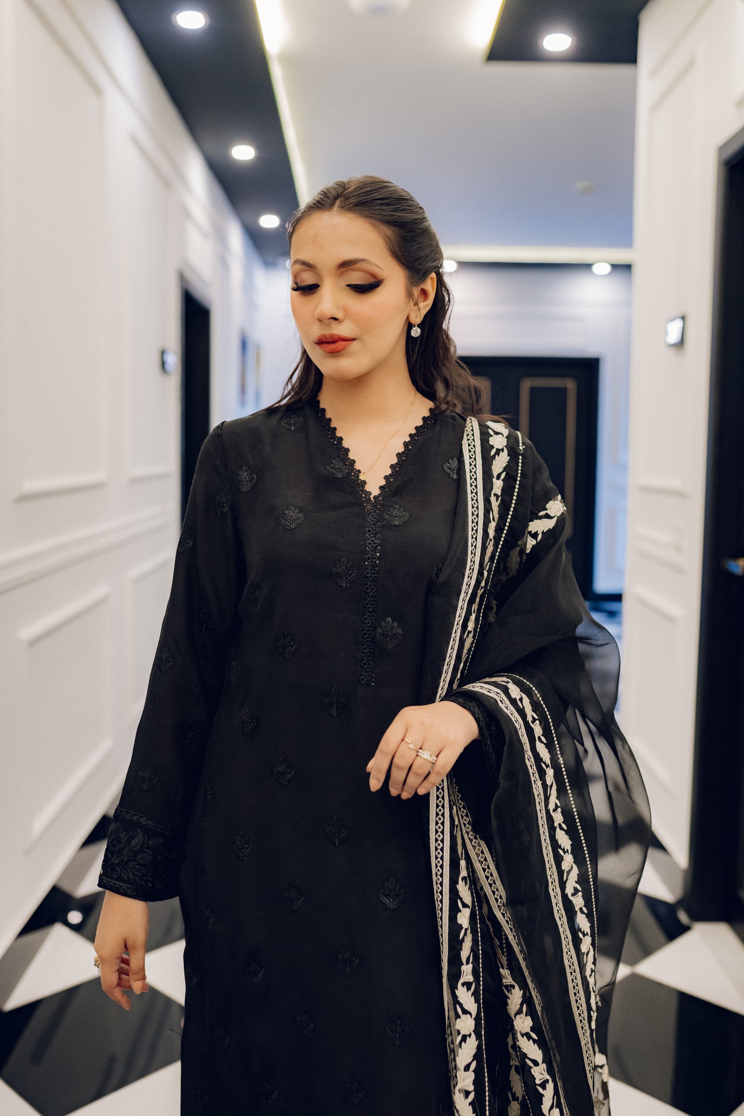 A sophisticated black embroidered dress with intricate motifs and lace detailing, paired with an organza dupatta featuring coordinated embroidery for an elegant look.