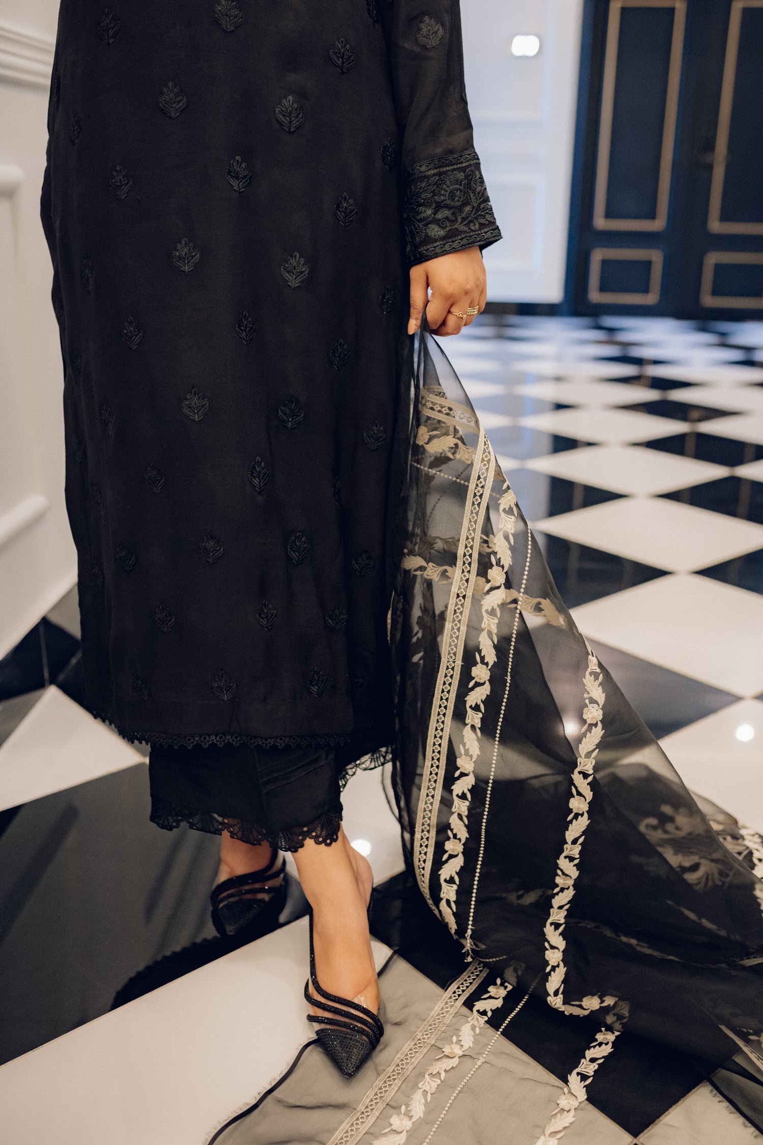 A sophisticated black embroidered dress with intricate motifs and lace detailing, paired with an organza dupatta featuring coordinated embroidery for an elegant look.