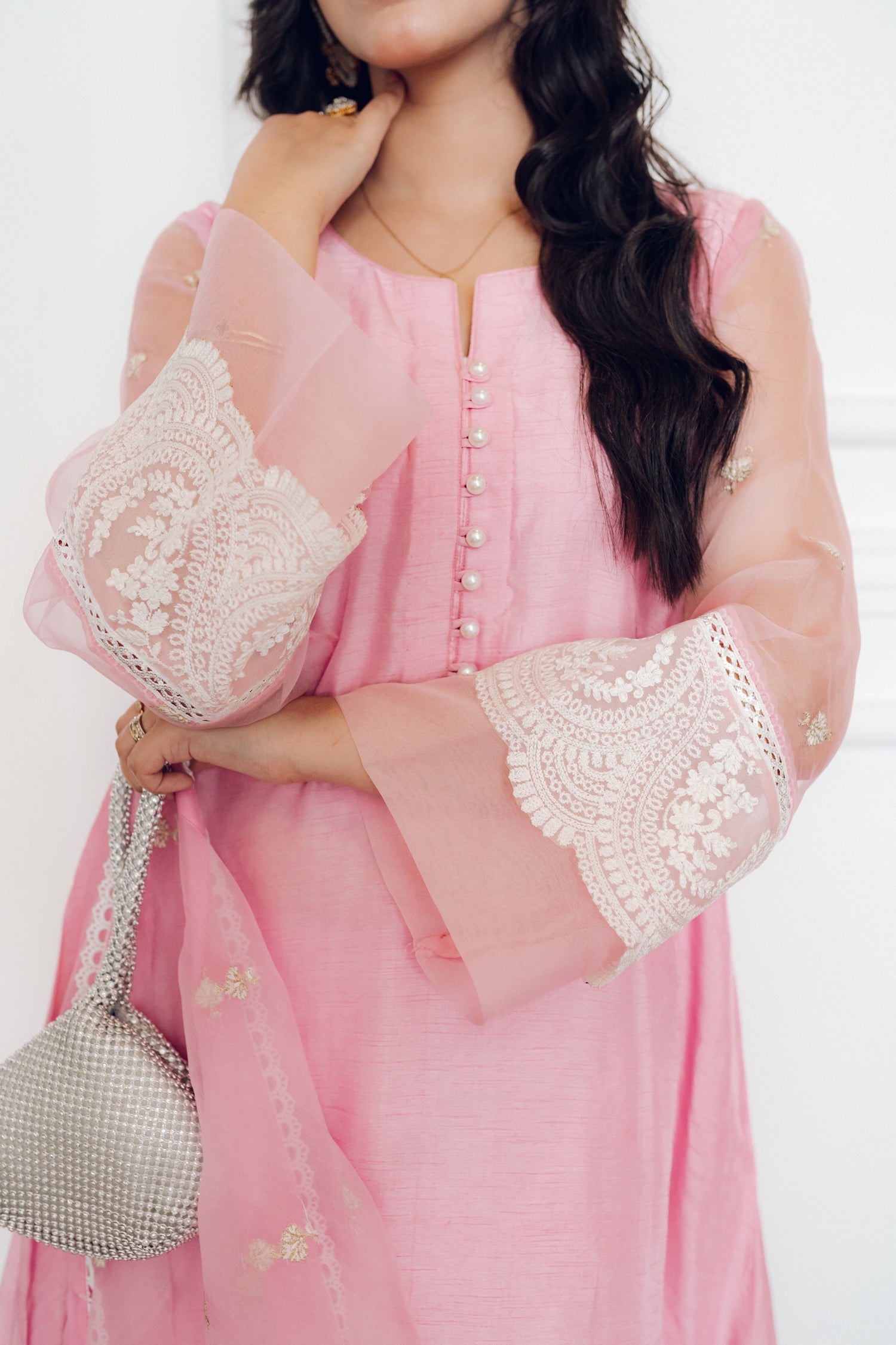A delicate pink dress adorned with lace and pearl buttons, exuding romance and timeless sophistication.