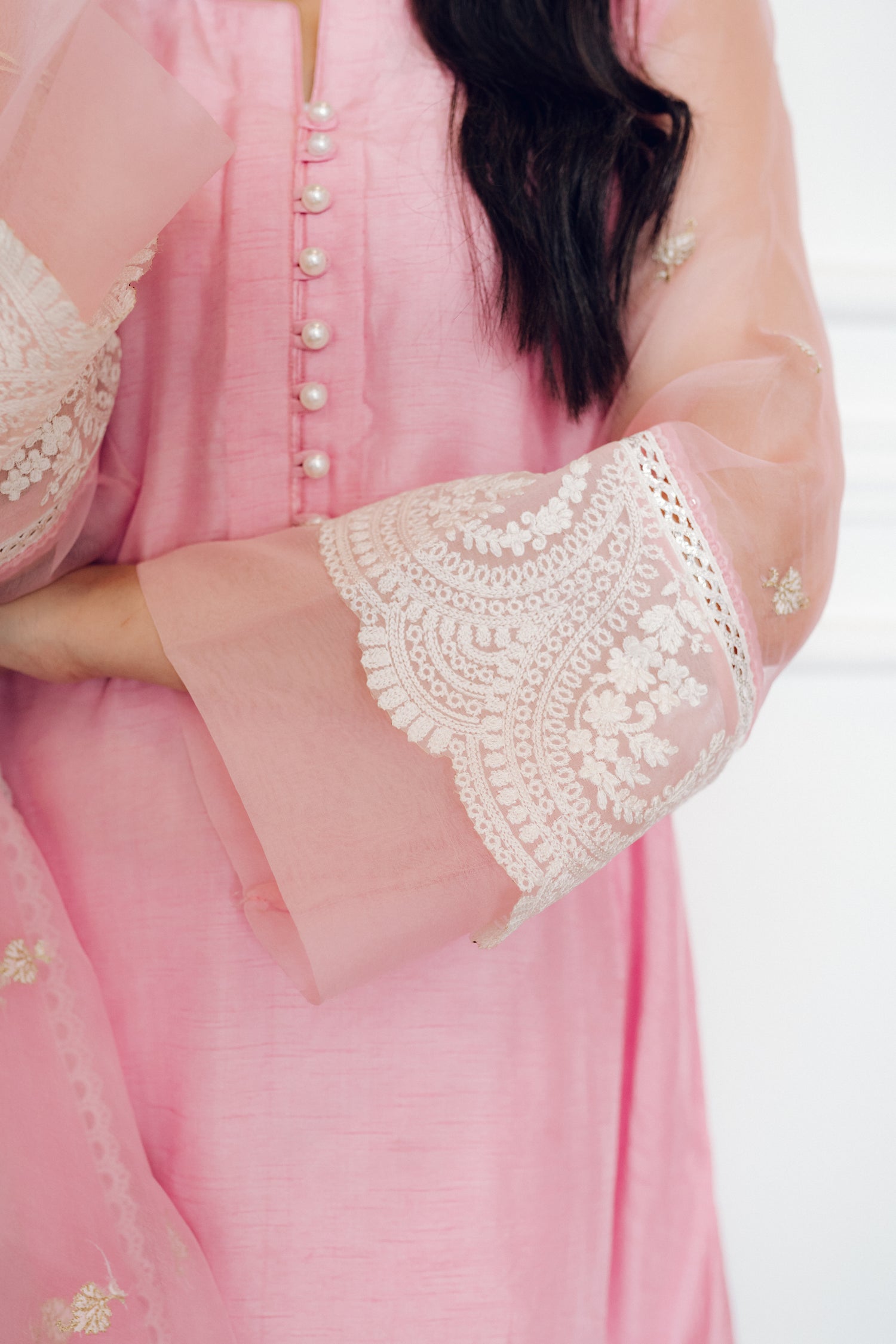 A delicate pink dress adorned with lace and pearl buttons, exuding romance and timeless sophistication.