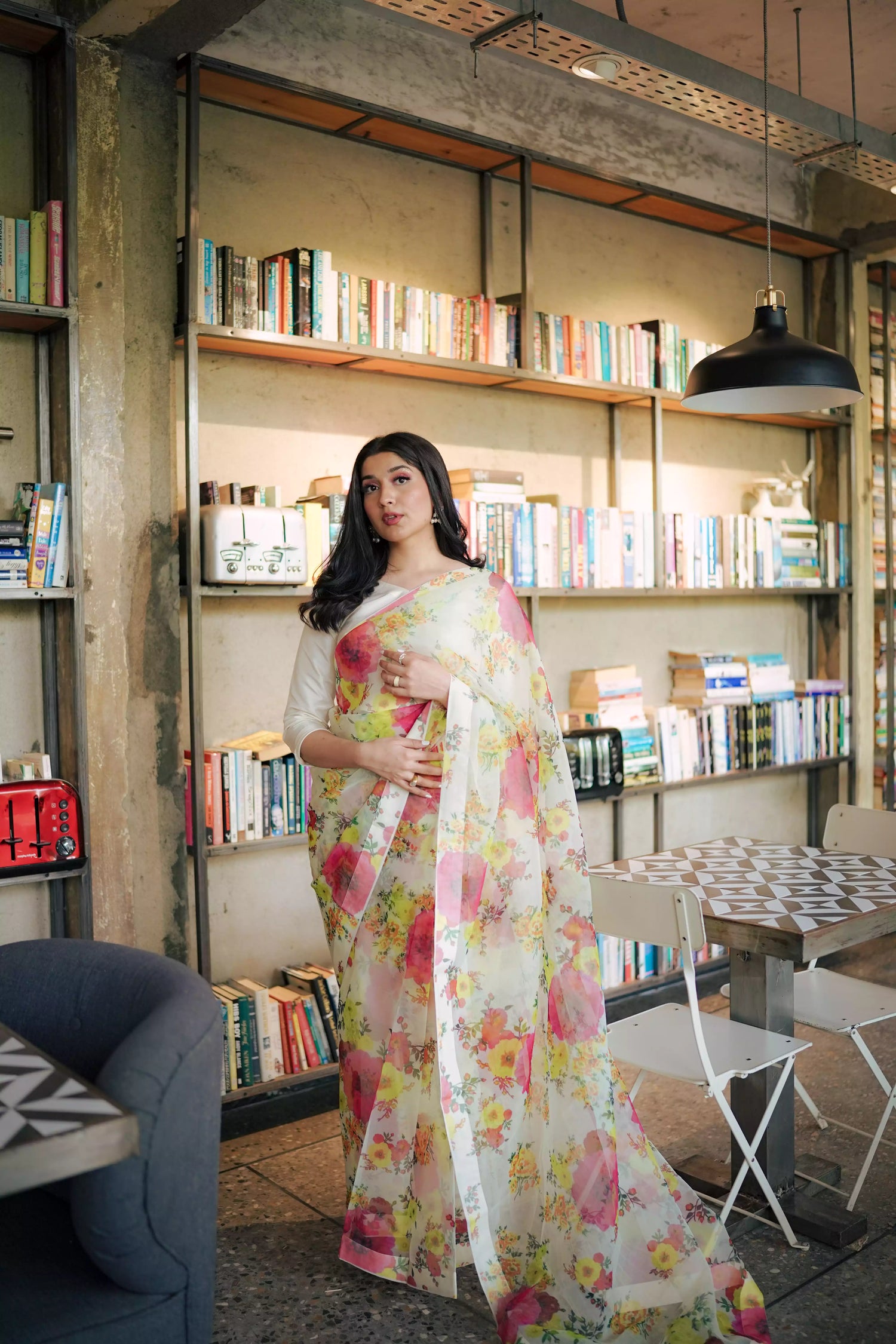 Cream floral printed organza saree with soft pastel patterns, paired with a matching Katan raw silk blouse and cotton petticoat; elegant drape ideal for festive and semi-formal occasions.
