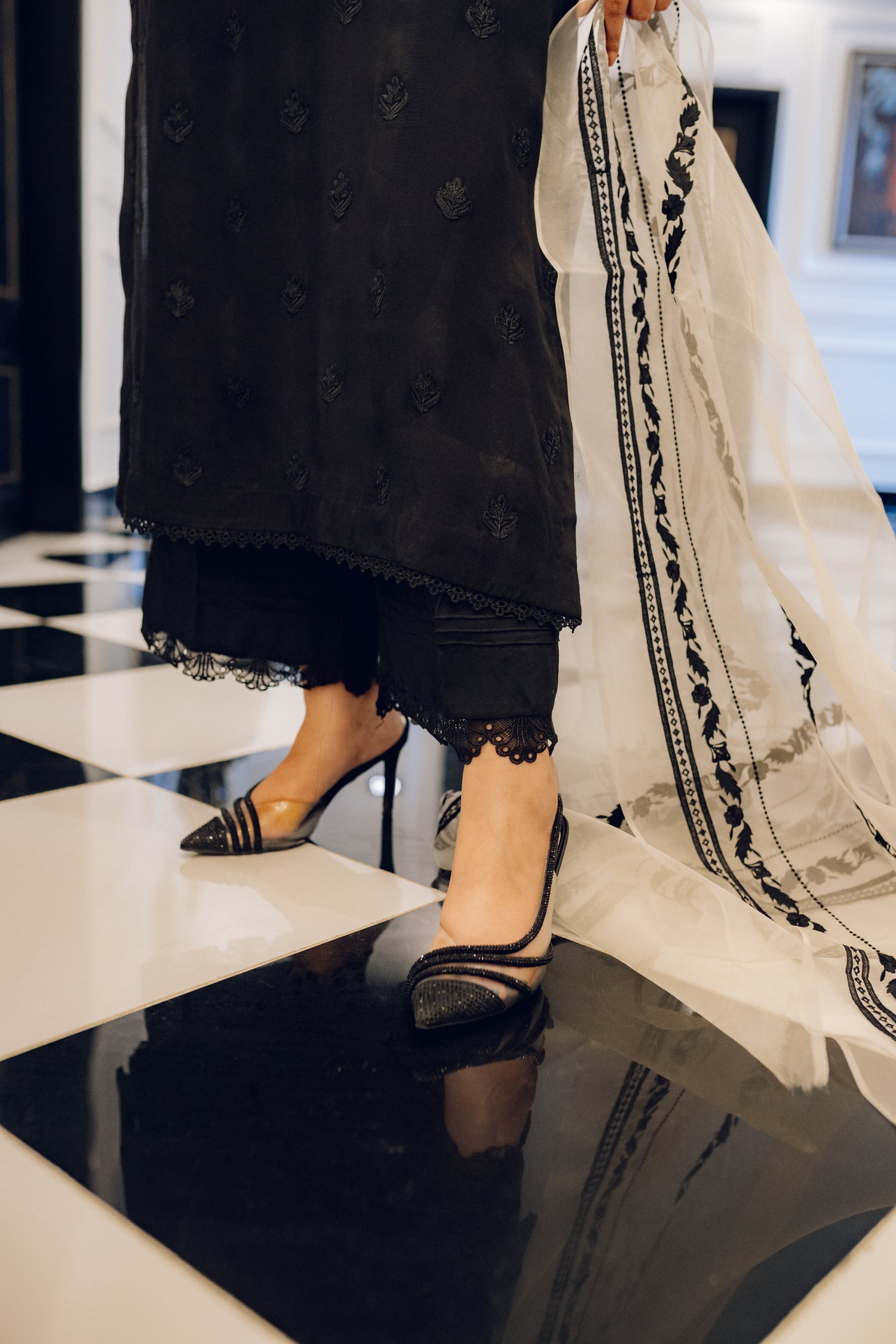 A black embroidered dress featuring celestial-inspired motifs and intricate lace detailing on the sleeves and pants, paired with a white organza dupatta adorned with coordinated embroidery for a refined, elegant contrast.