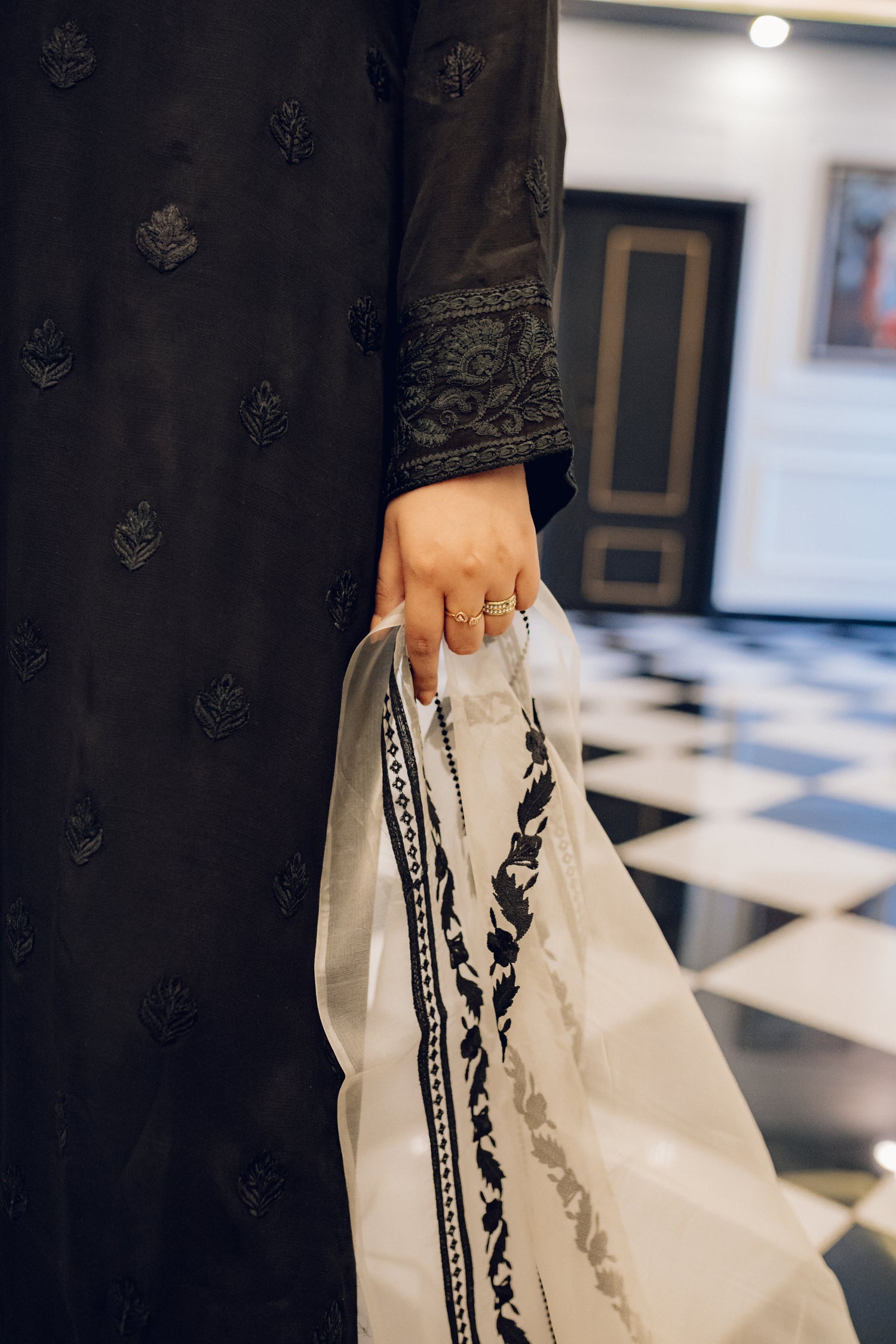 A black embroidered dress featuring celestial-inspired motifs and intricate lace detailing on the sleeves and pants, paired with a white organza dupatta adorned with coordinated embroidery for a refined, elegant contrast.