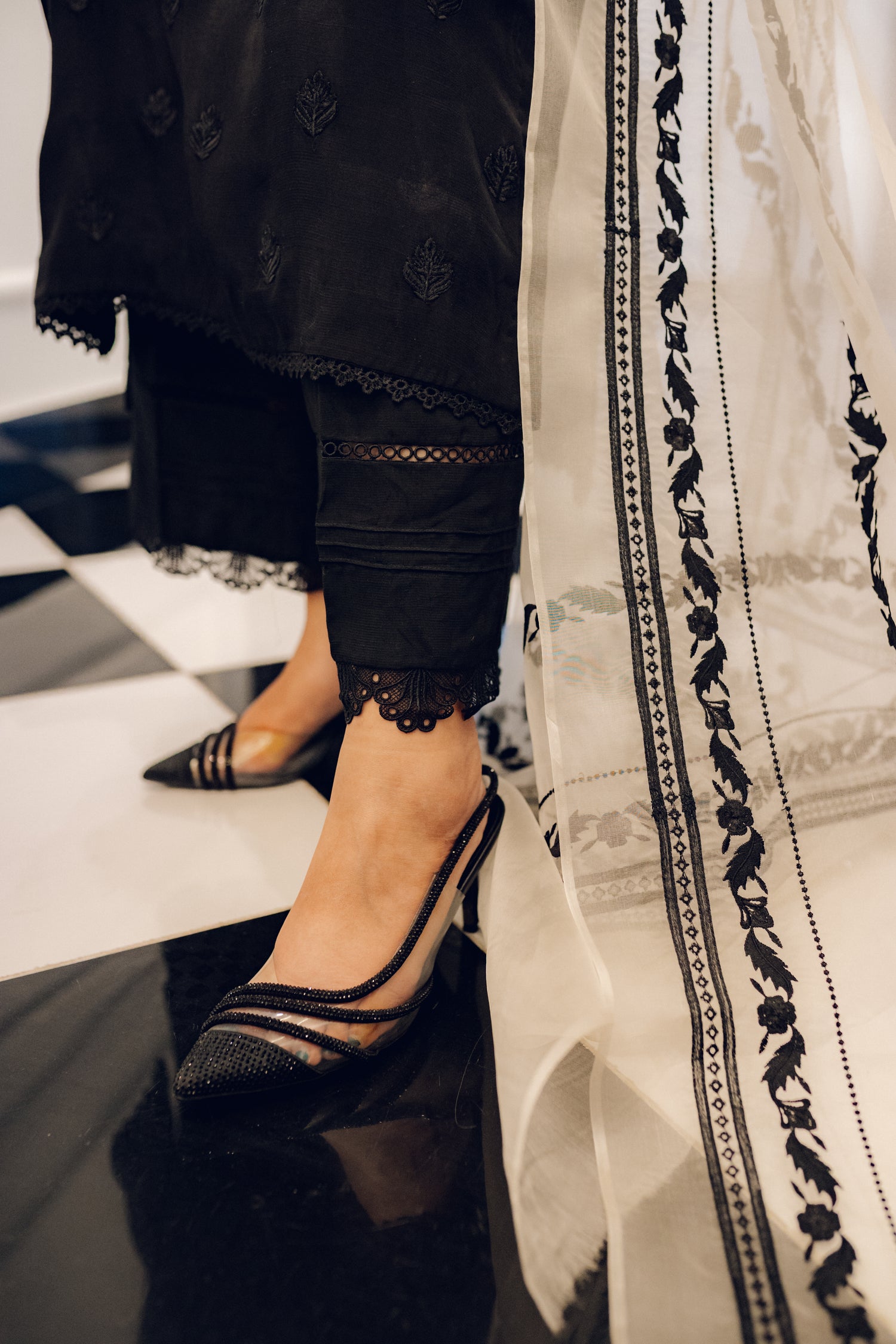 A black embroidered dress featuring celestial-inspired motifs and intricate lace detailing on the sleeves and pants, paired with a white organza dupatta adorned with coordinated embroidery for a refined, elegant contrast.