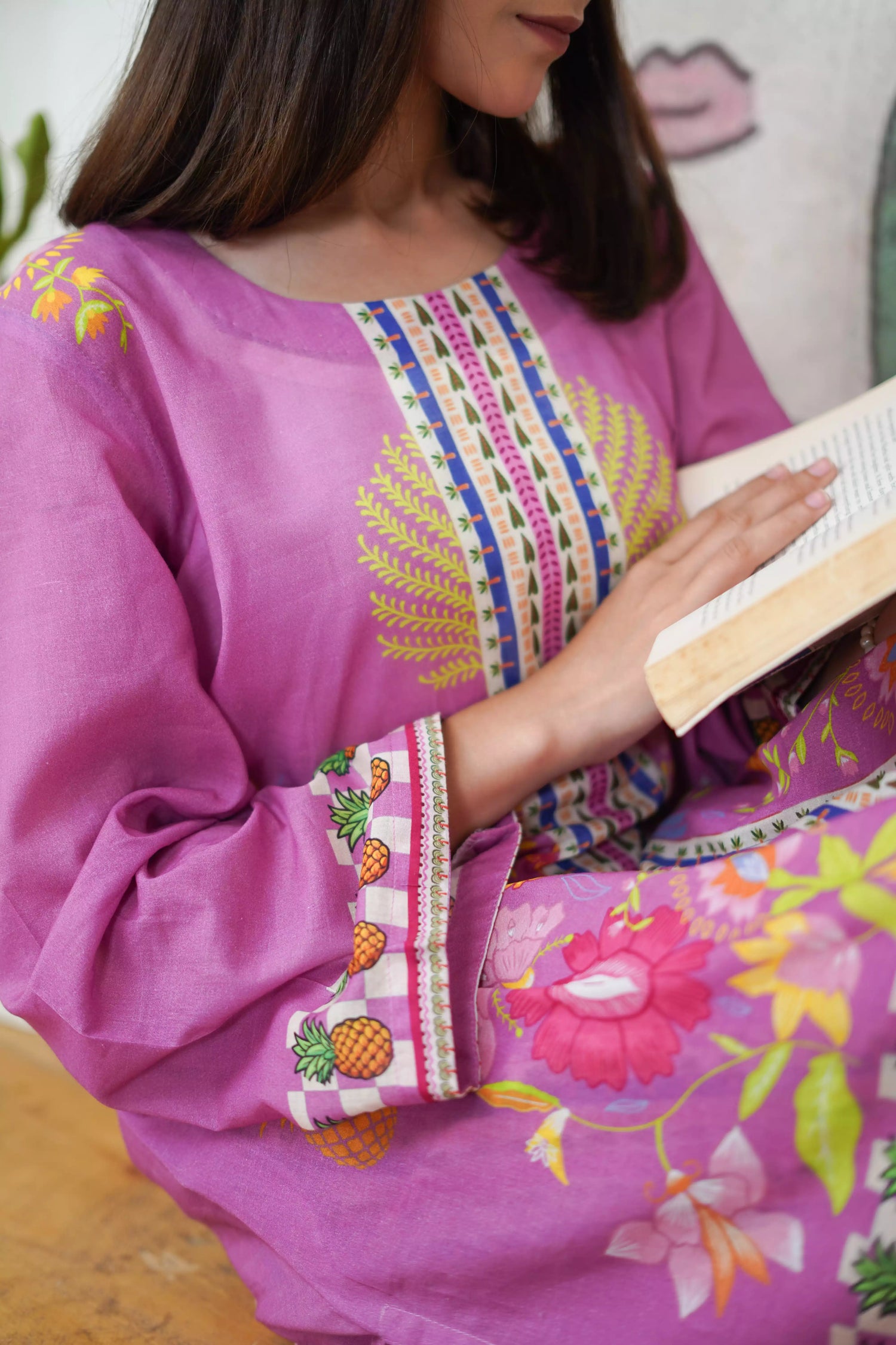 Person wearing a vibrant pink traditional outfit with colorful embroidery, holding a book.