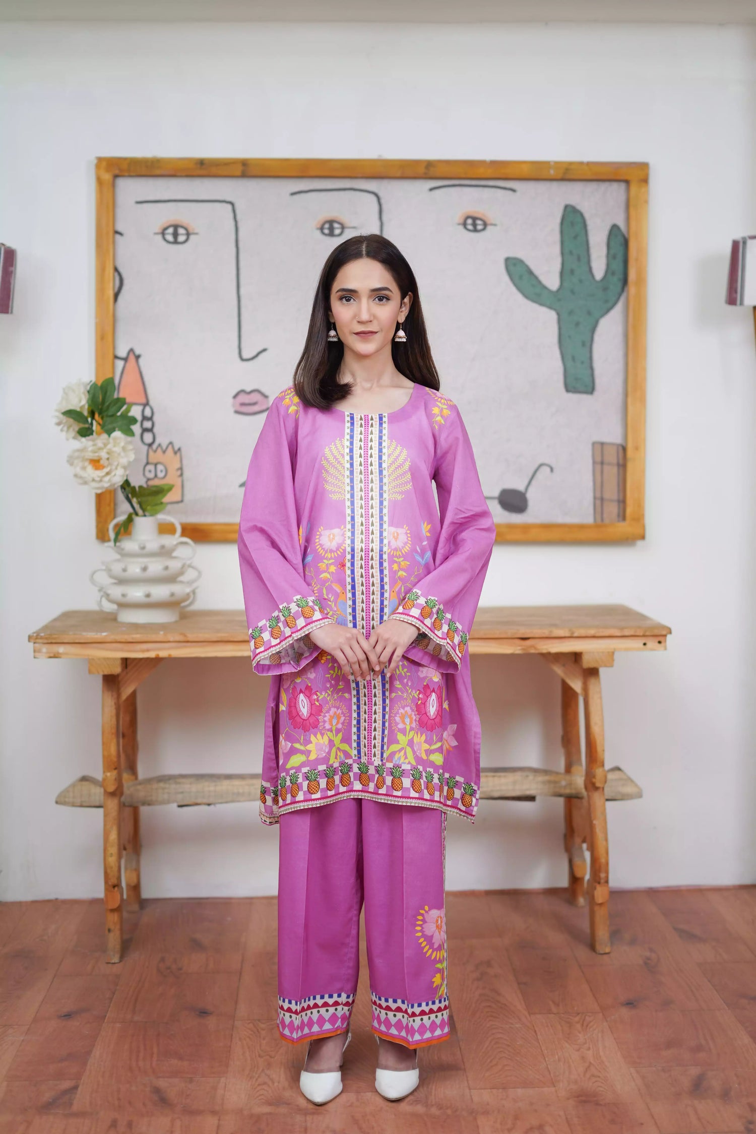 Woman wearing a pink embroidered outfit standing in front of a wall with a cactus painting.