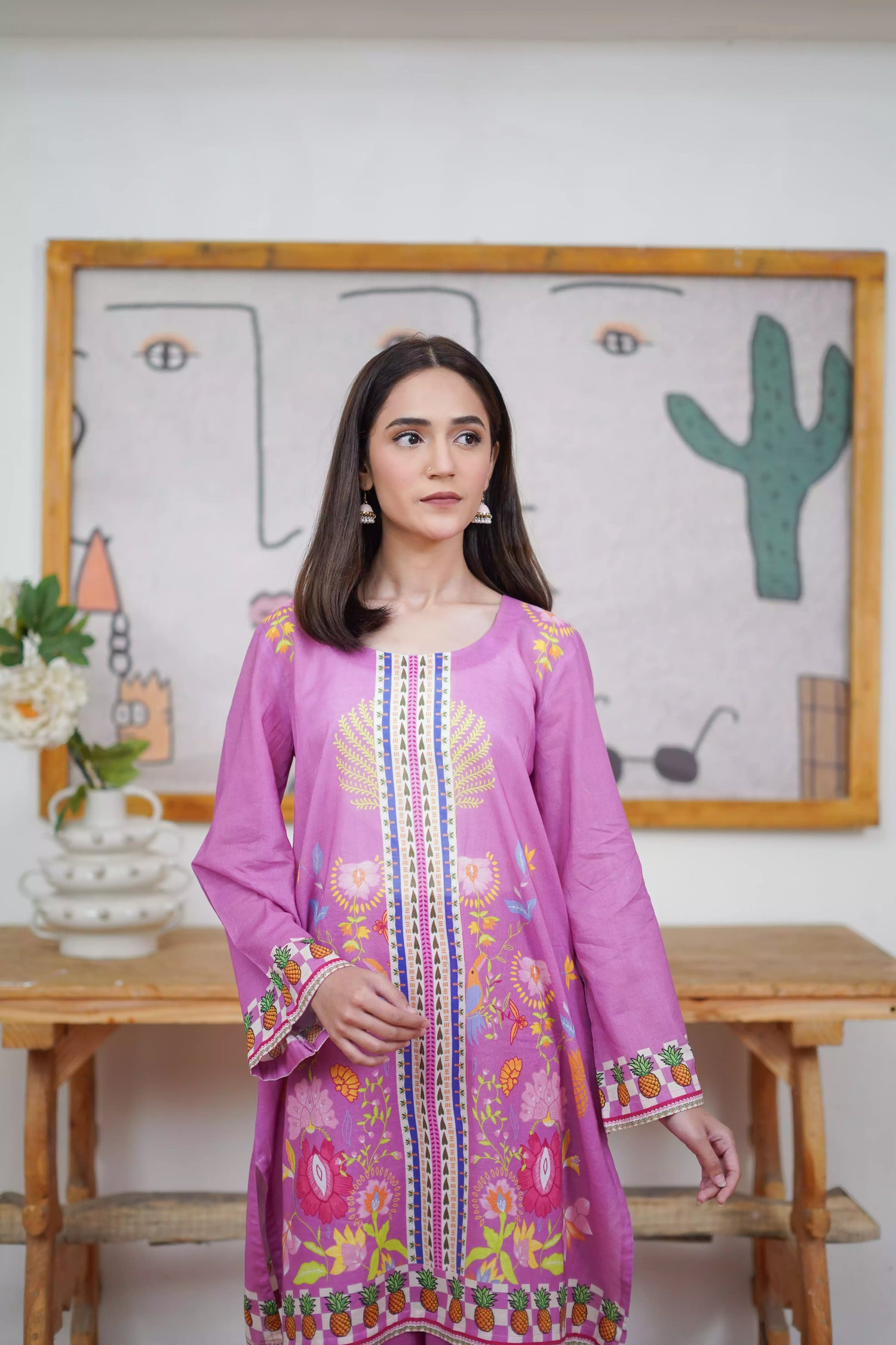 Woman wearing a purple embroidered dress standing in front of a wall with a cactus painting.