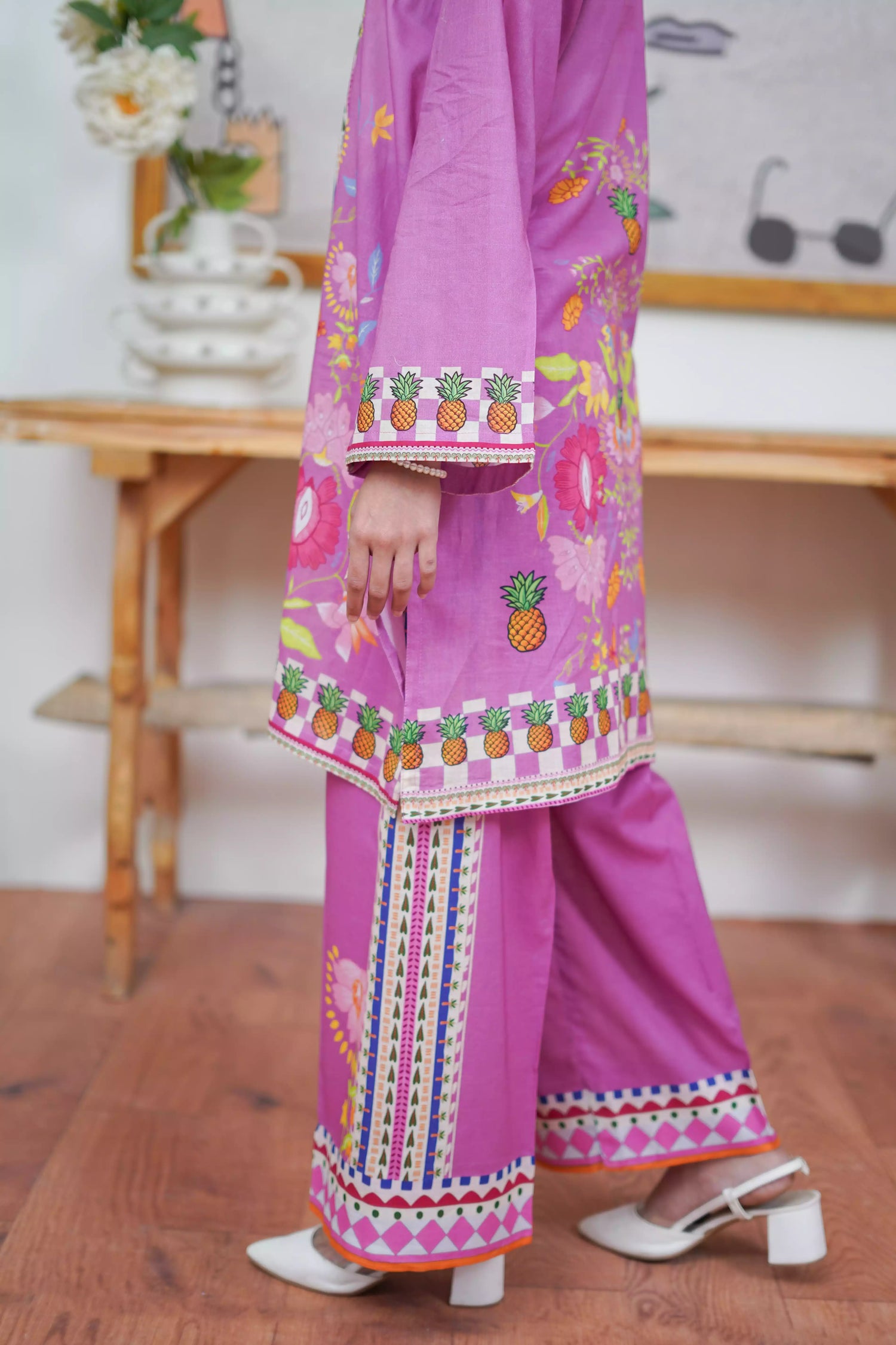 Person wearing a vibrant pink traditional outfit with pineapple patterns on a wooden floor.