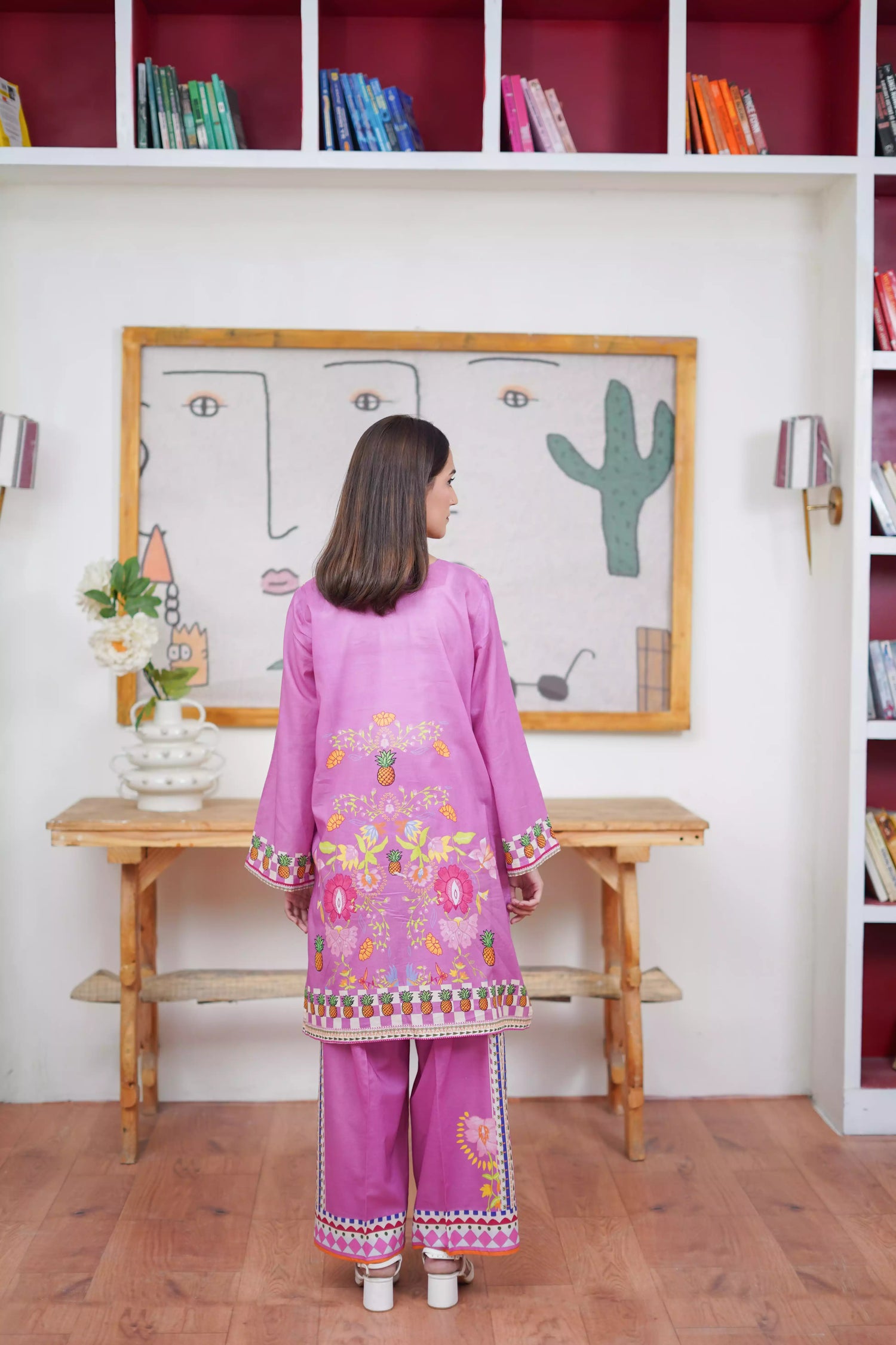 Woman in a purple embroidered outfit standing in a room with a whiteboard and shelves.
