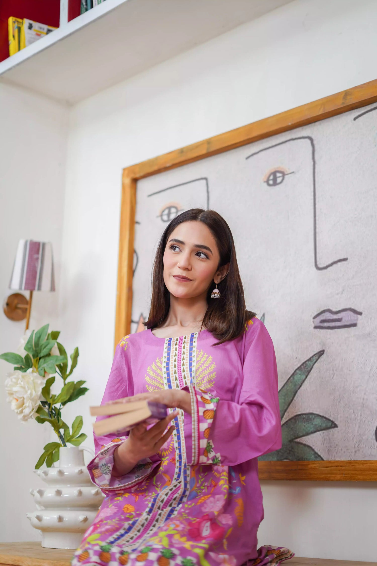 Woman in a colorful dress standing in a room with a painting on the wall.