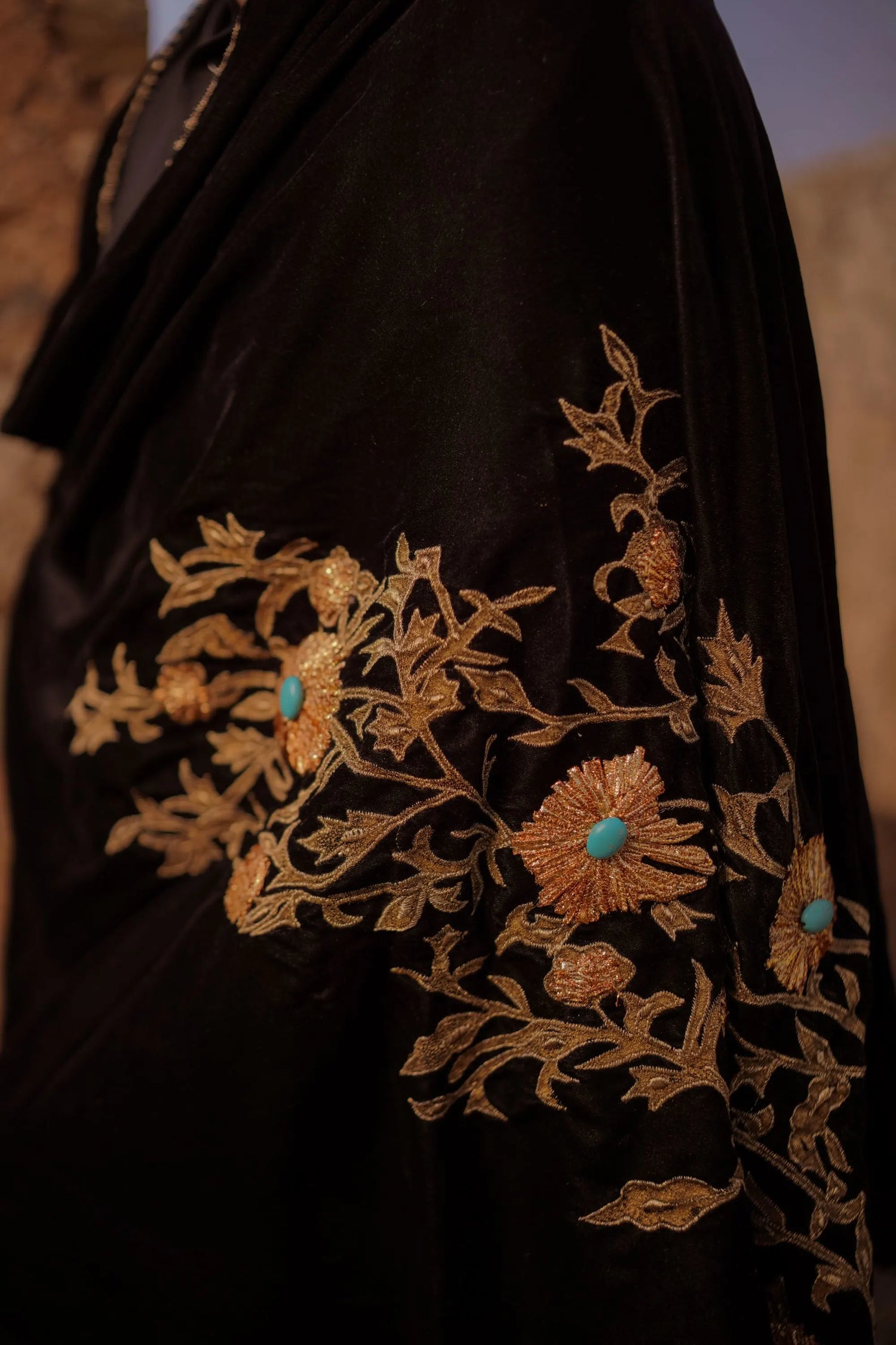 A velvet shawl adored with tila embroidery, feroza stone work and block printed floral motifs, embodying a blend of elegance and traditional charm.